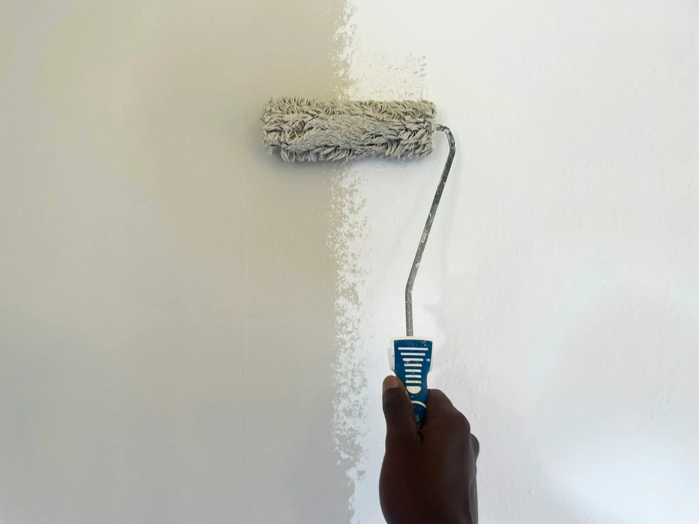 Rolo de pintura aplicando tinta branca em parede